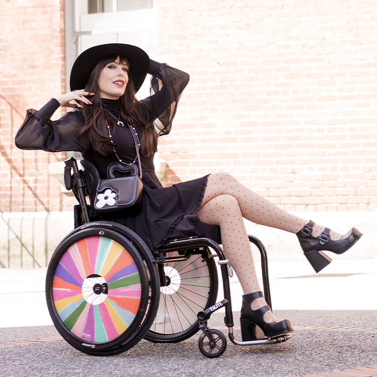 Tara Moss poses wearing the black and white Luciana bag and black Vogtalk Dionna platform heels. Her wheelchair has colourful rainbow wheels.